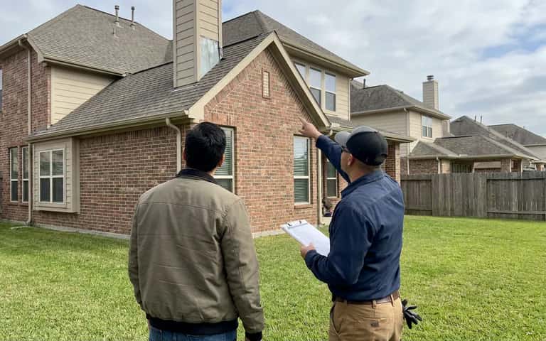 Inspector pointing out a roofline detail to a homebuyer outside a two-story house