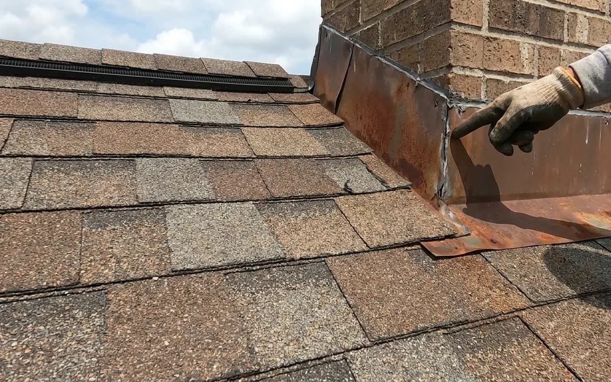 Inspector pointing at chimney flashing on a shingle roof