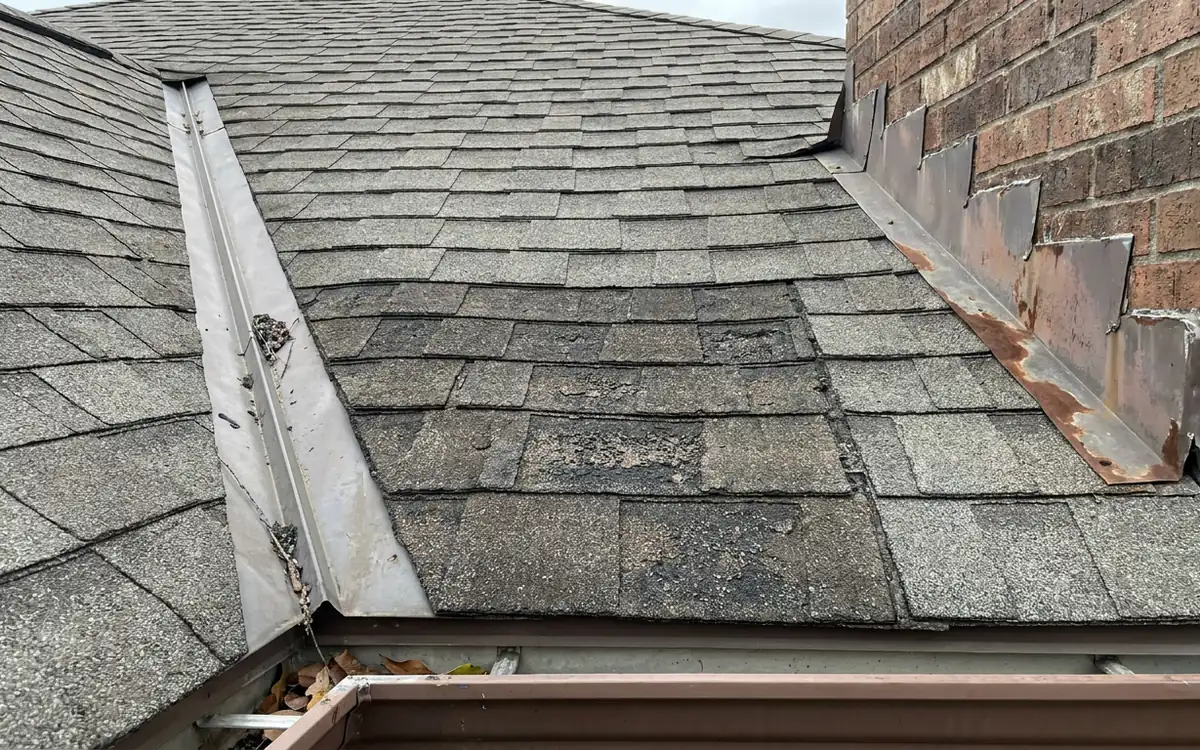 Roof valley and wall flashing with weathered shingles above a gutter