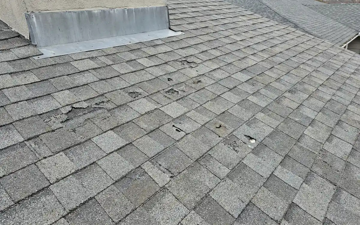Gray shingle roof with scattered impact marks and metal flashing