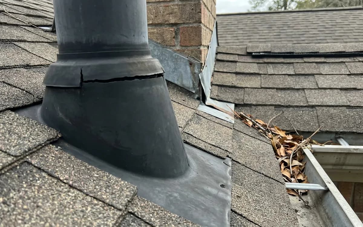 Cracked pipe boot seal and roof flashing beside leaves in a gutter