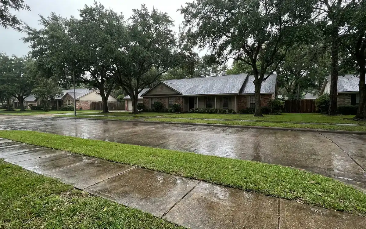 Rain-damp Tomball suburban roofline viewed from sidewalk