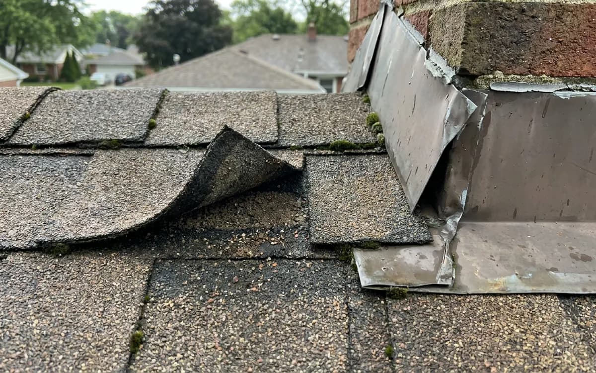 Wind-lifted shingle edge and flashing detail assessed after weather exposure