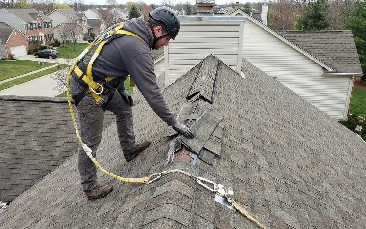 Roofing professional inspecting ridge shingles and flashing for storm damage